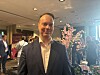 Lahden kaupunginhallituksen puheenjohtaja Pekka Komu pukuun pukeutuneena tapahtumatilassa, taustalla ihmisiä ja kukkia.