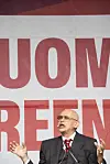 Jorma Uotinen puhuu lavalla punavalkoisen taustakankaan edessä Suomi Areena-tapahtumassa.