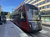 Punainen Tampereen ratikka pysäkillä kaupunkikadulla rakennusten reunustamana.